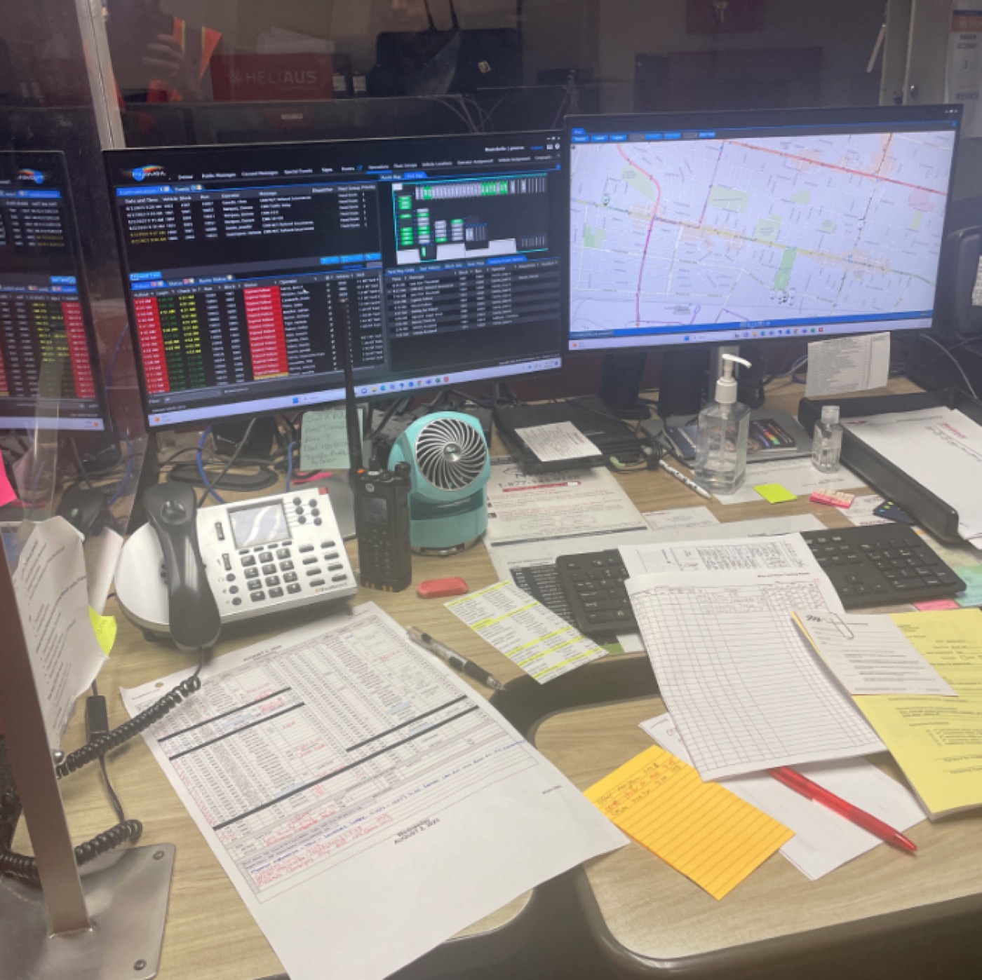 A control desk buried in paper, sticky notes, a radio and a phone next to live screens